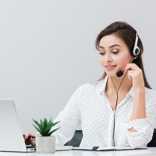 A woman with a headset sits at a desk, focused on her laptop, engaged in work or a virtual meeting.